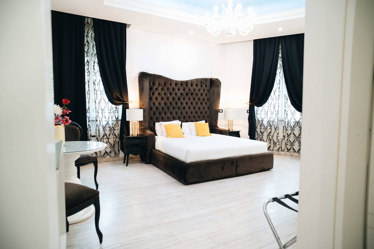 Ein Schlafzimmer mit einem großen Bett, zwei Nachttischen, einem Sessel und einem kleinen Tisch mit Blumen.