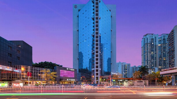 Ein modernes Hochhaus mit markant vertikaler Gestaltung, umgeben von weiteren Hochhäusern und einer belebten Stadtstraße bei Abenddämmerung.