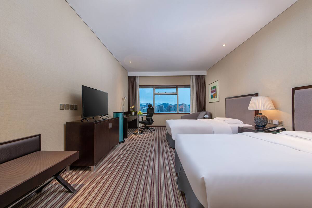 Hotelkamer met twee bedden, een bureau met een televisie, bureaulamp en een raam met uitzicht op de stad.