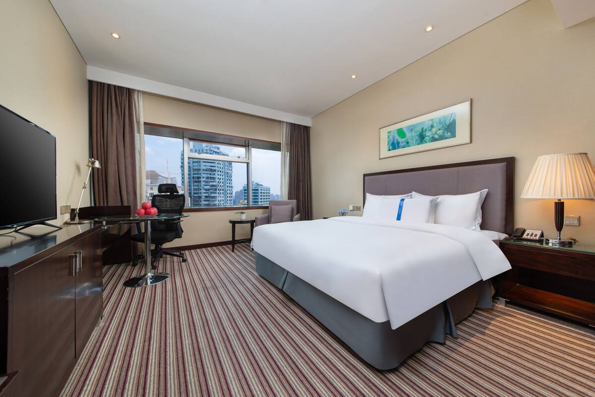 Een hotelkamer met een groot bed, een bureau met een computer, een televisie en een raam met uitzicht over de stad.