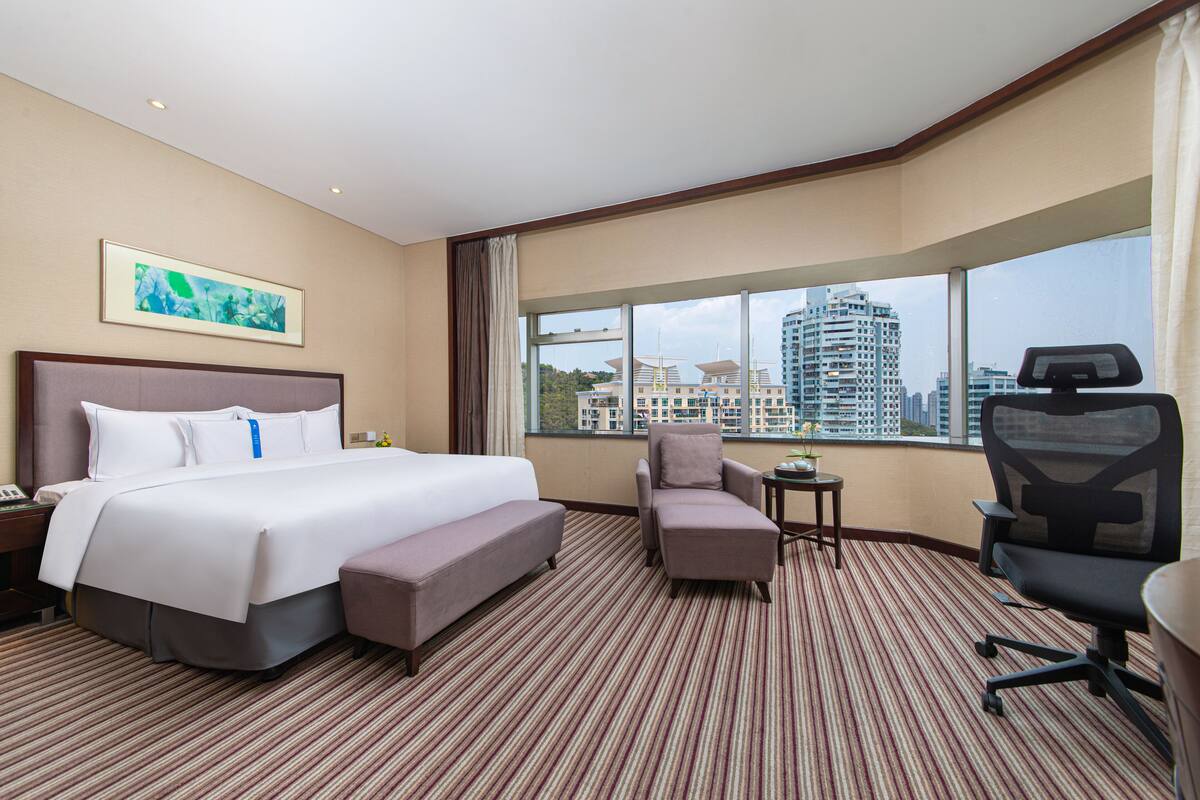 Een hotelkamer met een groot bed, een bureau, een stoel en uitzicht op een stadsbeeld.