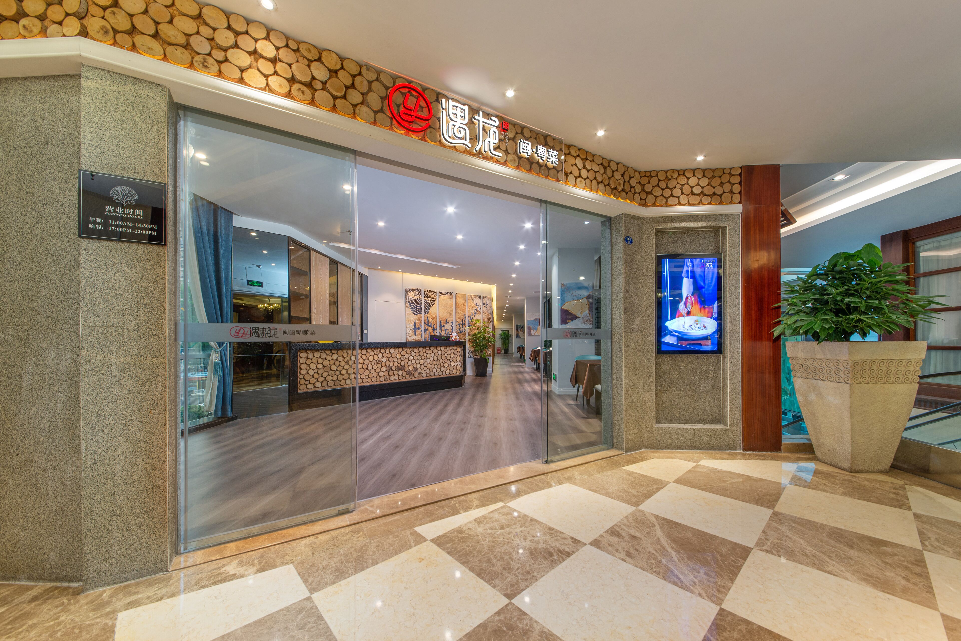 Entrada de un hotel con mostrador de recepción y una planta grande en maceta.