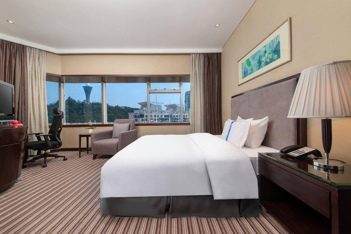 Hotelkamer met een groot bed, een bureau, een stoel, een televisie, een lamp en een raam met uitzicht over de stad.