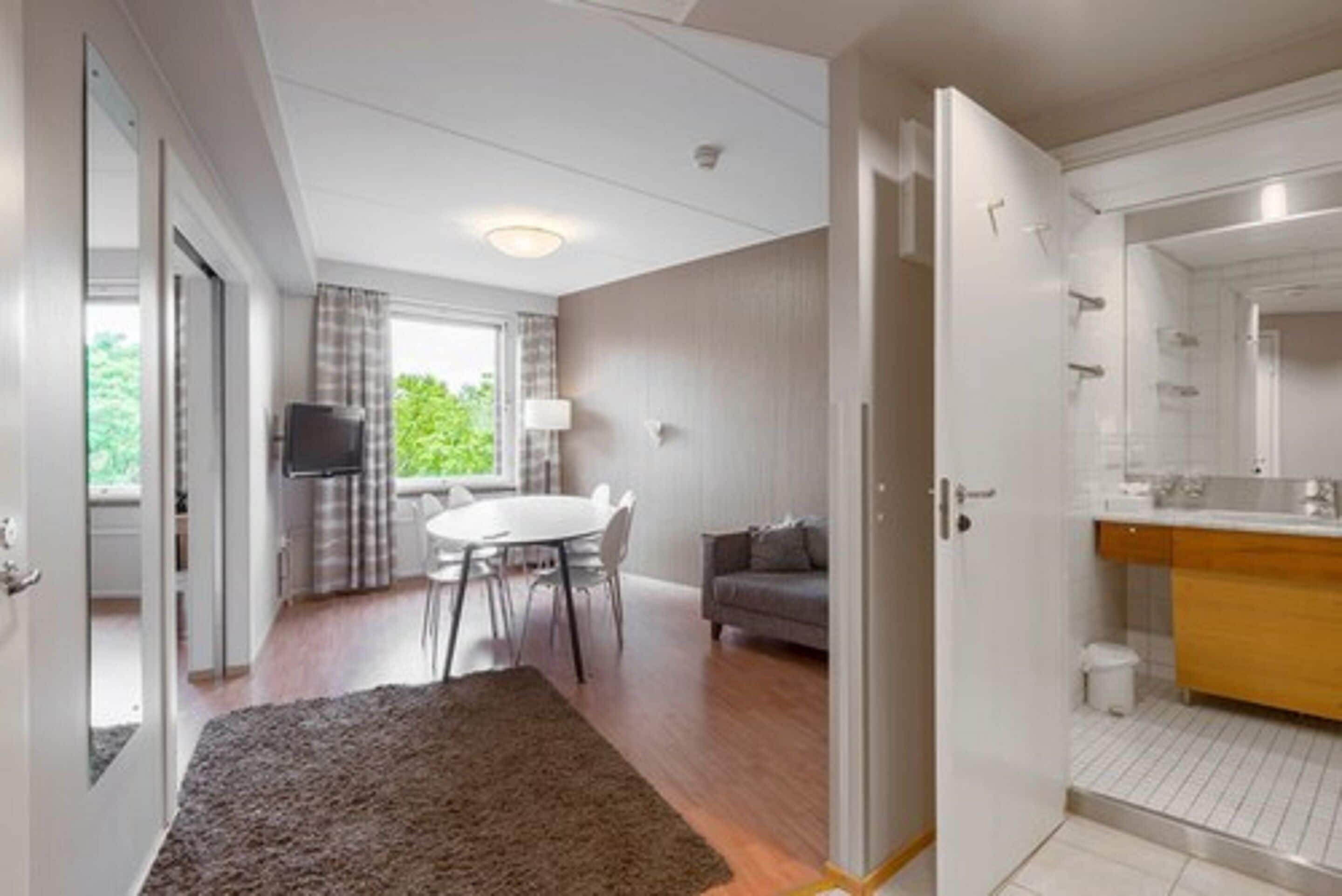 A modern hotel room with a dining area, a sofa, and a bathroom with a mirror and sink.