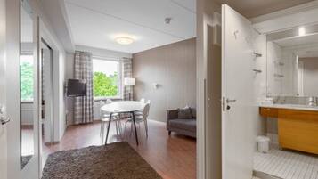 A modern hotel room with a dining area, a sofa, and a bathroom with a mirror and sink.