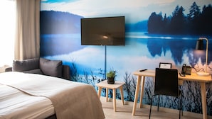 Una camera d'albergo con un letto, una scrivania con una sedia, una televisione e un affresco raffigurante un lago.