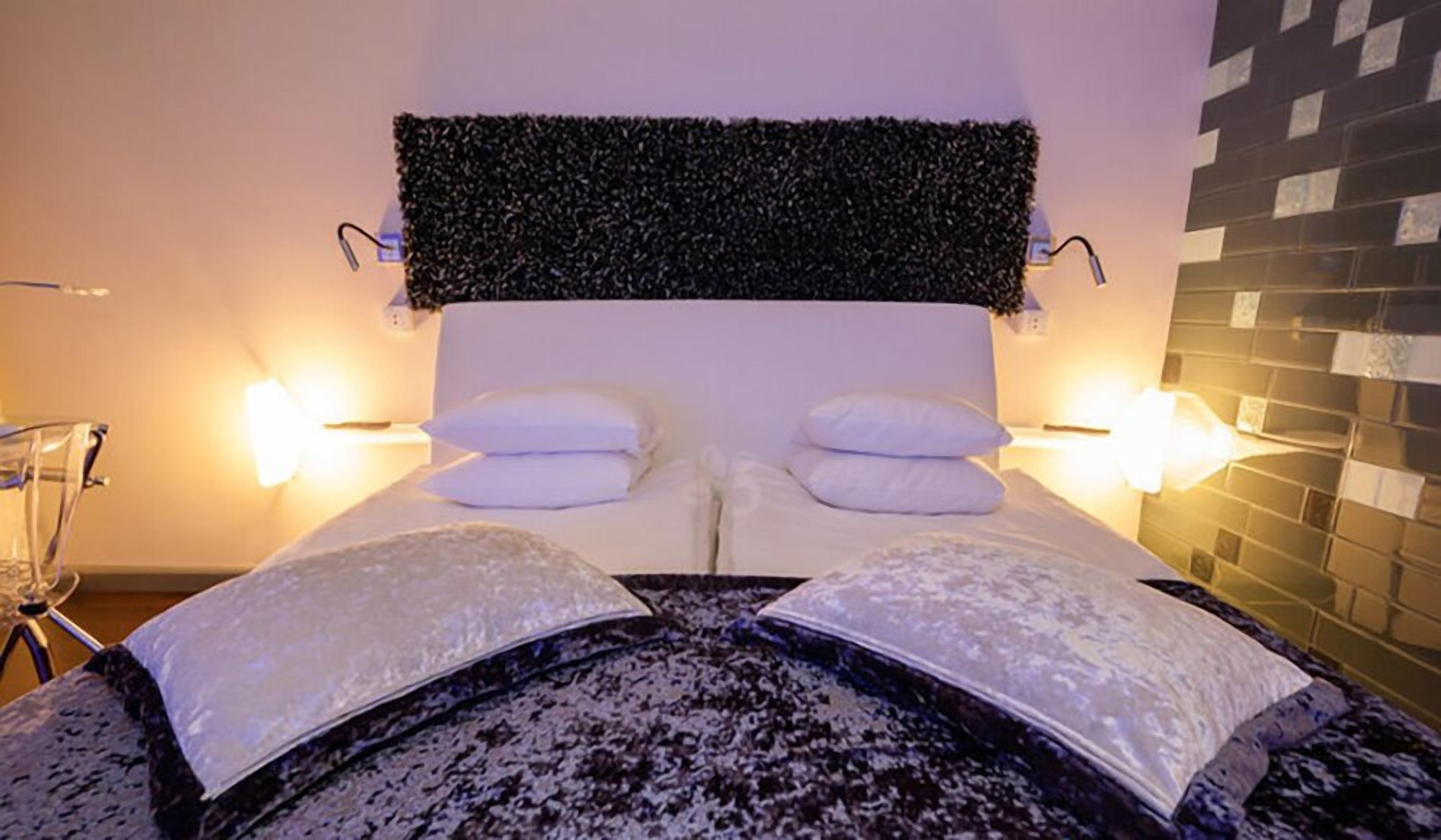 Et hotelværelse med en stor seng, to sengeborde med lamper og en dekorativ vægpanel.