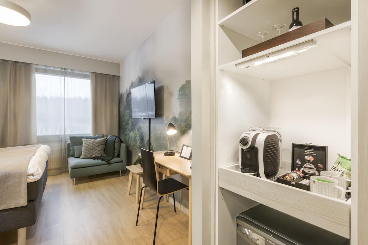 Una habitación de hotel moderna con una cama, un sofá, un escritorio con lámpara, un televisor y una cafetera.