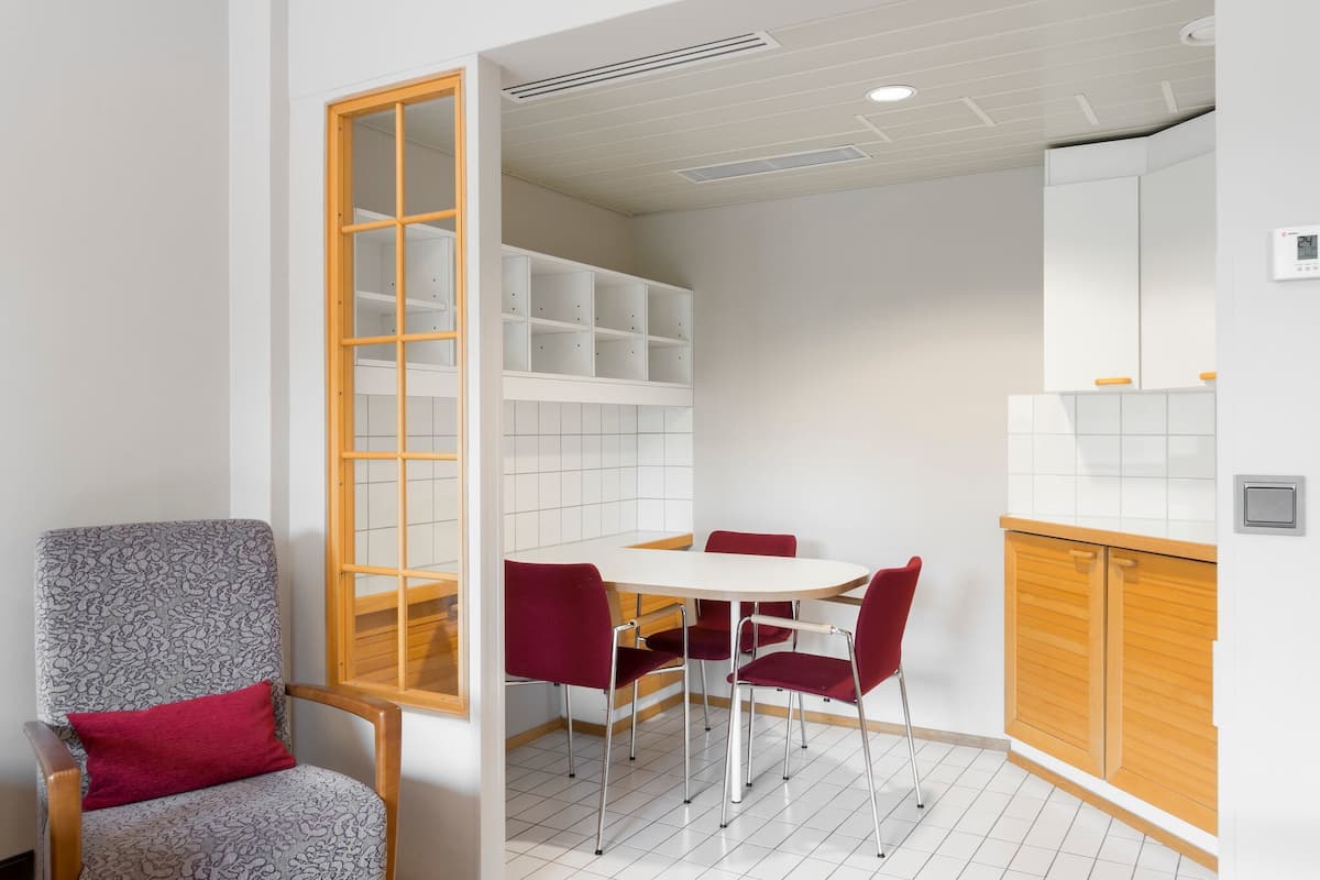 Una cocina pequeña y moderna con armarios blancos, encimera de madera y una zona de comedor con mesa blanca y sillas rojas.
