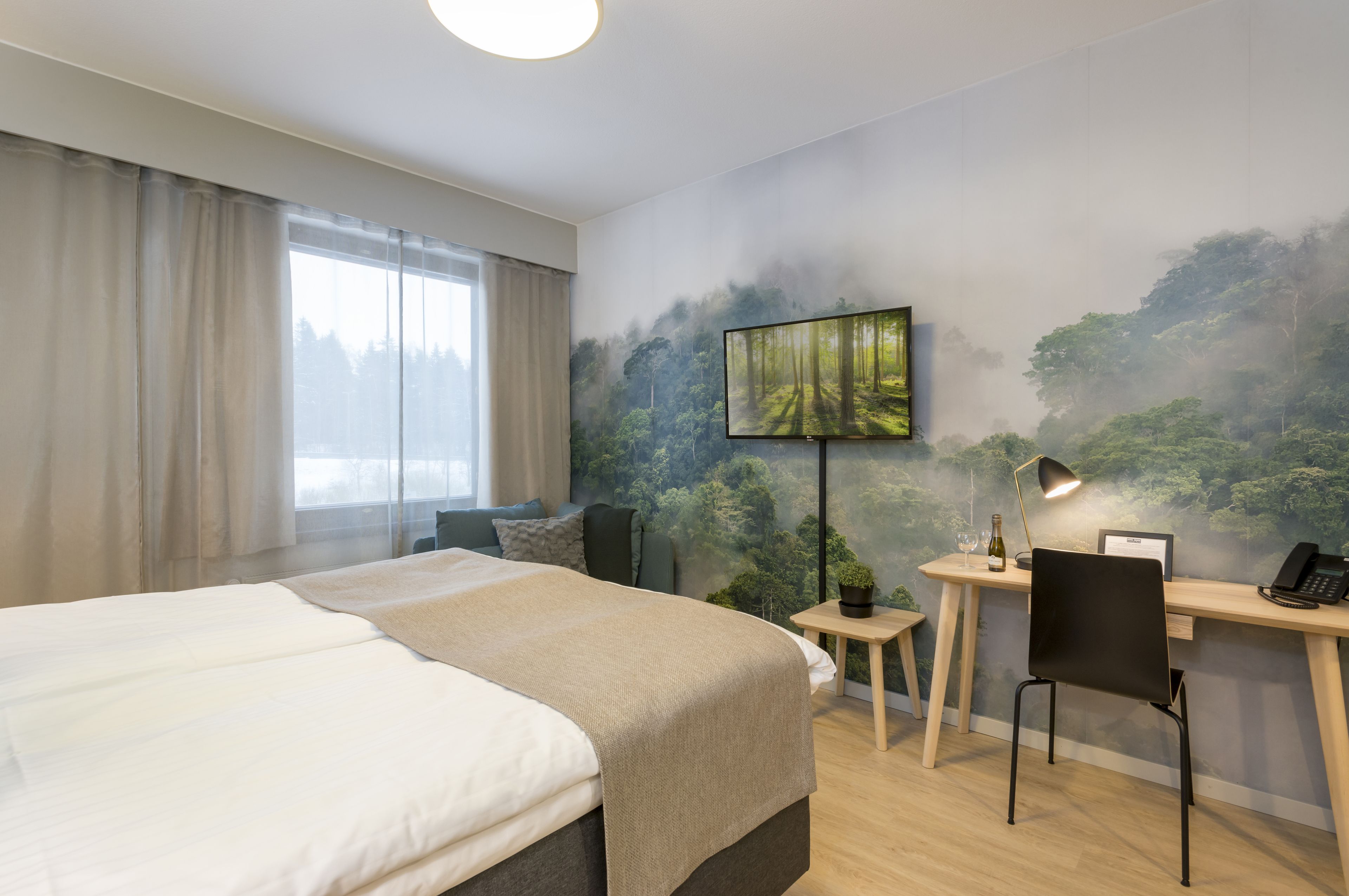 A hotel room with a bed, a desk, a chair, a TV, and a window with curtains.