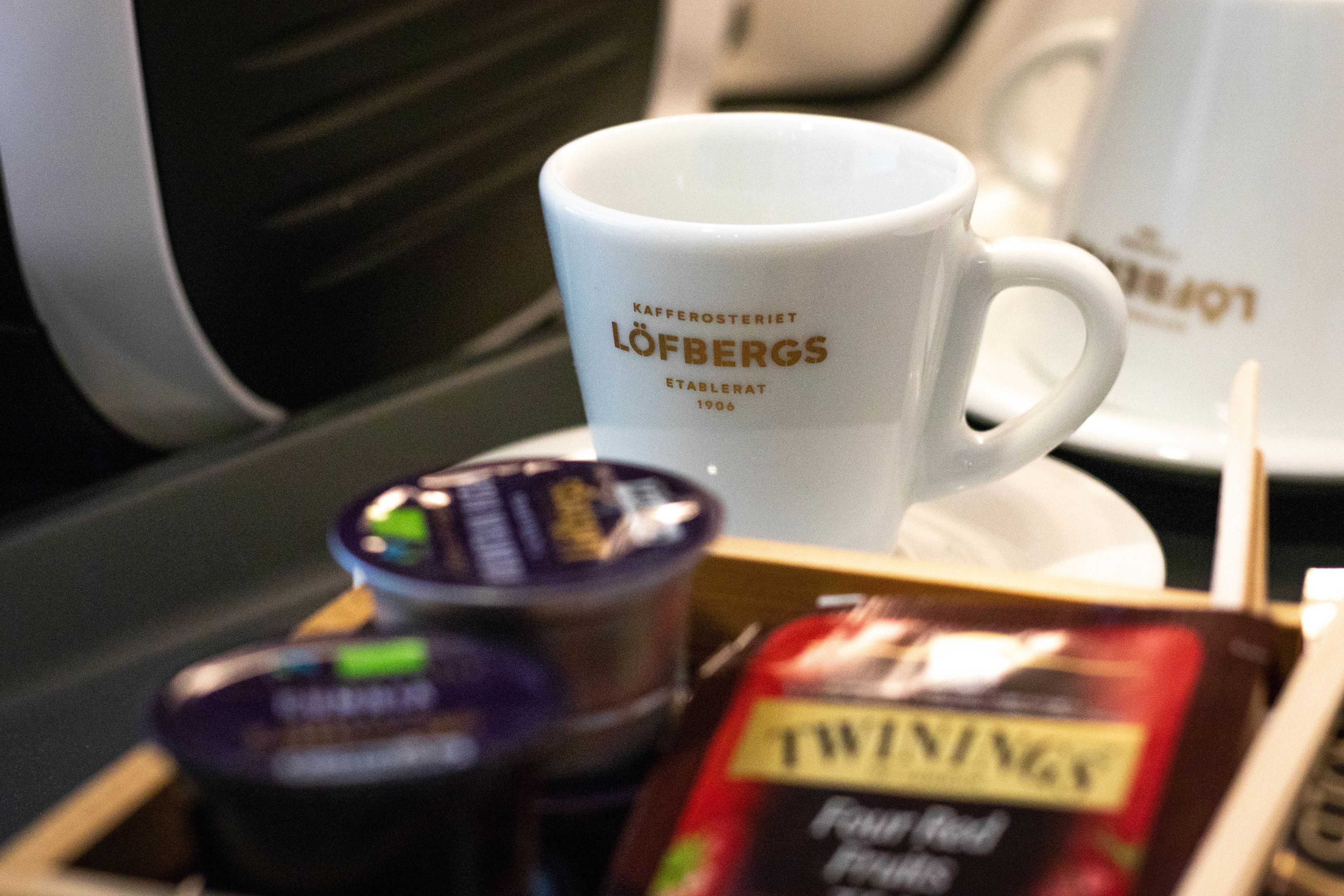 Eine weiße Kaffeetasse mit Aufschrift, eine kleine Dose und eine Packung Twinings Tee.