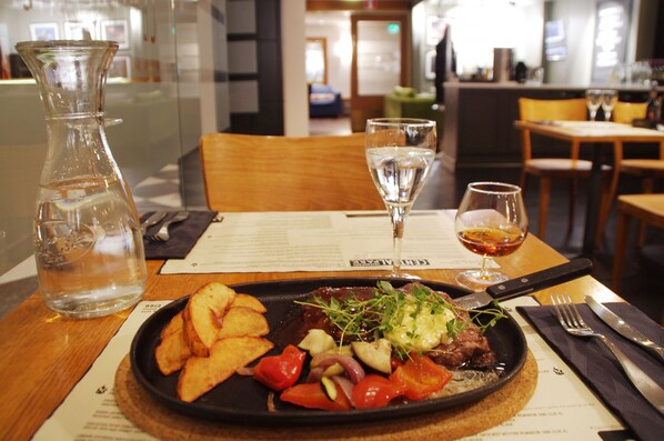 A restaurant setting with a table set for a meal, including a plate of food, a glass of water, and a menu. - Hotel Haaga Central Park (Helsinki)