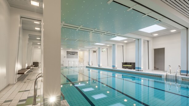 Una grande piscina interna con acqua cristallina, pareti piastrellate e un moderno design del soffitto.