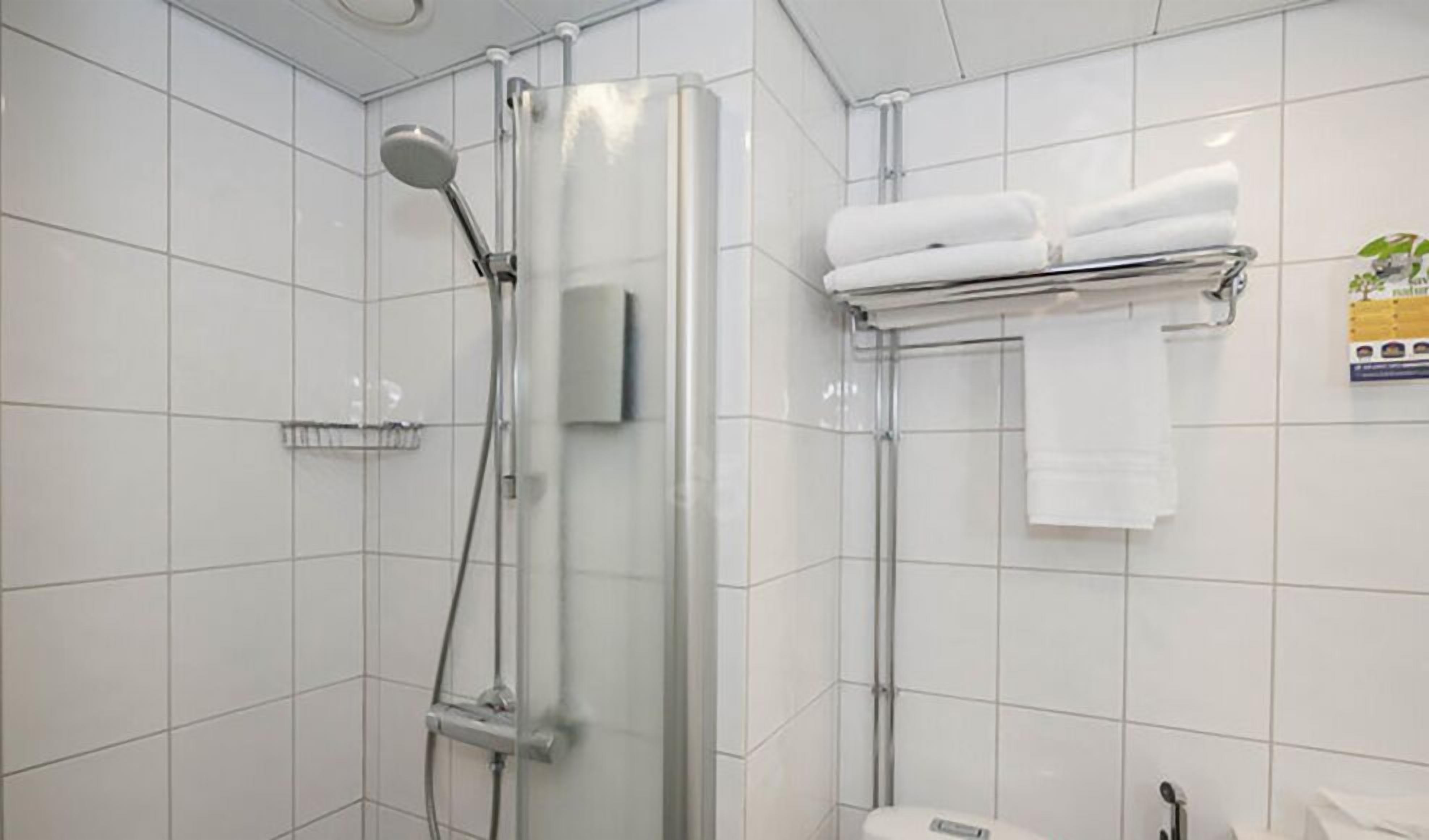 A modern bathroom with white tiles, a glass-enclosed shower, a towel rack with folded towels, and a visible hand dryer.
