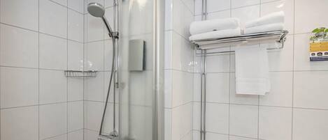 Un baño moderno con azulejos blancos, una ducha con mampara de vidrio, un perchero con toallas dobladas y un secamanos visible.