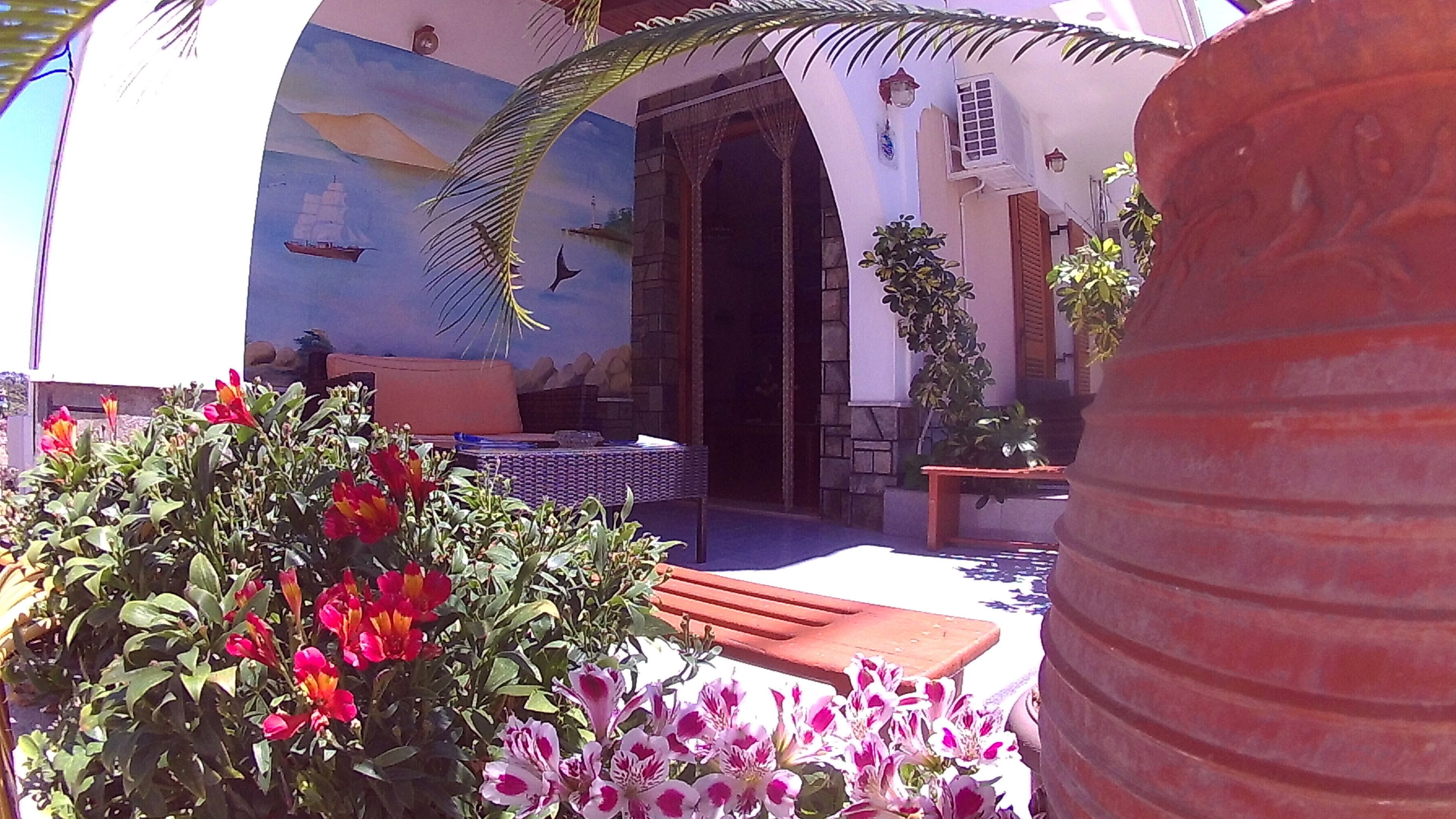 Un patio con zona de comedor, un mural y plantas en macetas.