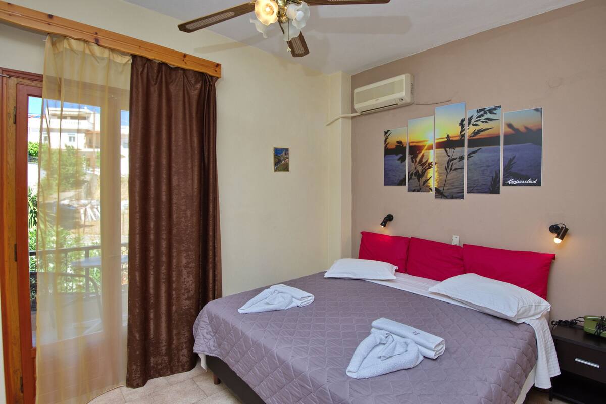A bedroom with a bed, a ceiling fan, a window with curtains, and wall art.