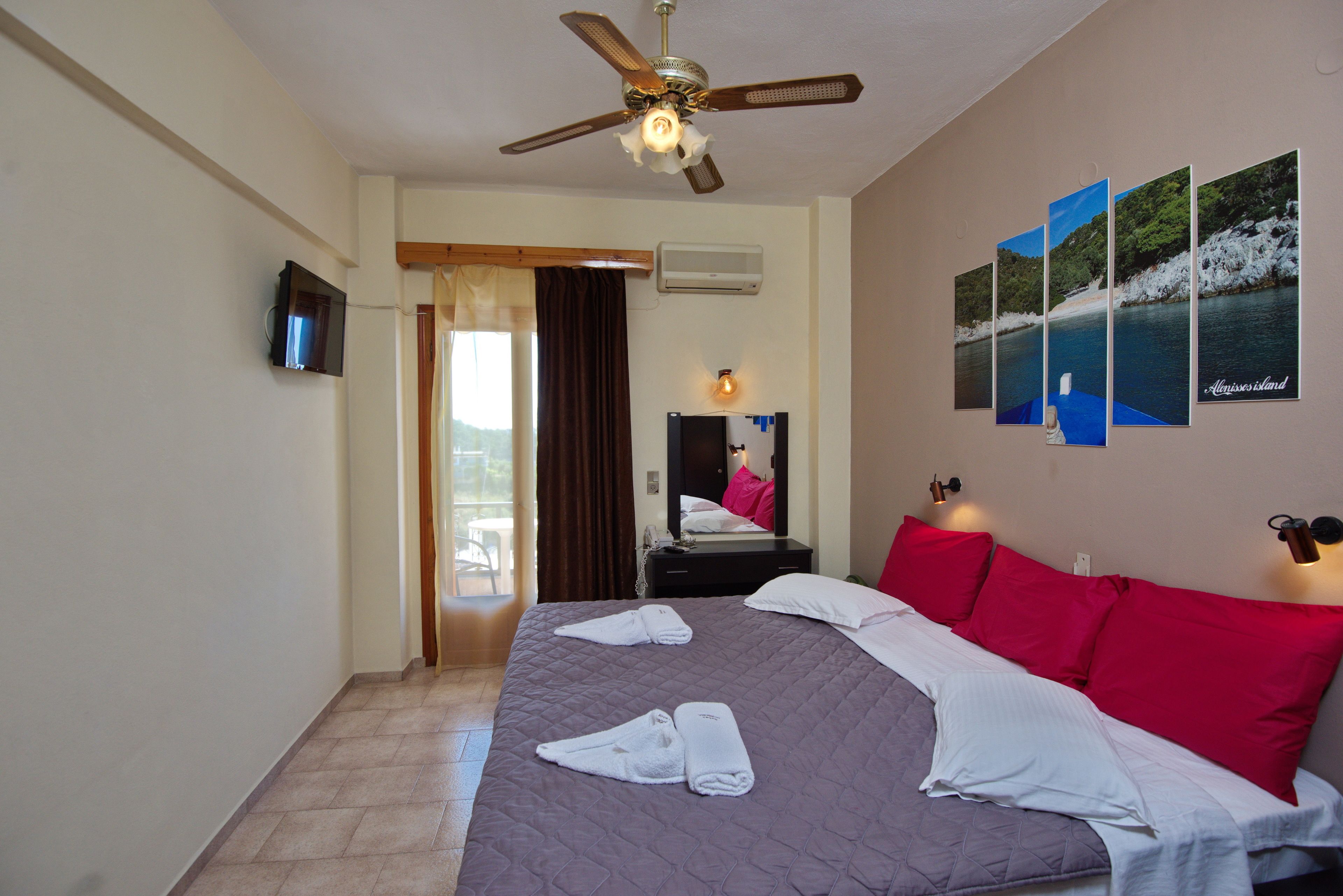 Ein Hotelzimmer mit Bett, Deckenventilator, Fernseher, Spiegel und einem Fenster mit Vorhängen.