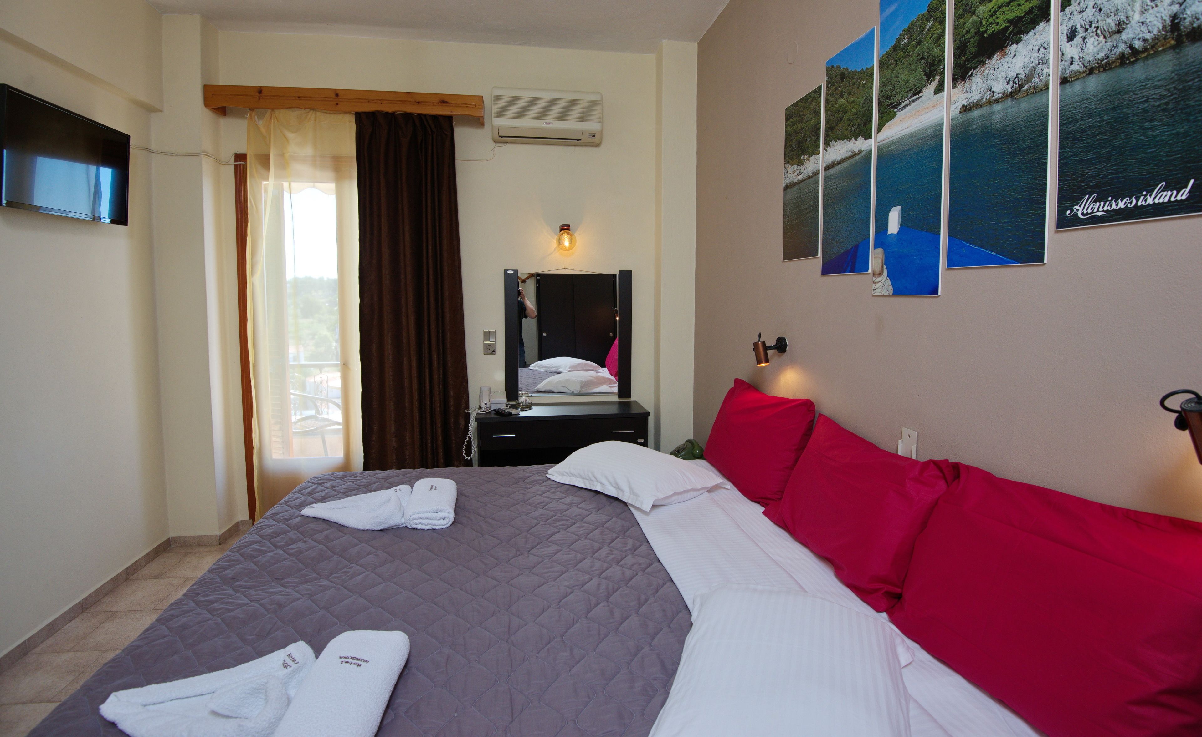 Une chambre d’hôtel avec un lit, un miroir, un bureau avec un téléphone et un mur orné de tableaux.