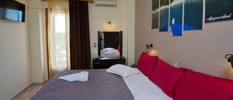 A hotel room with a bed, a mirror, a desk with a telephone, and a wall with framed pictures.