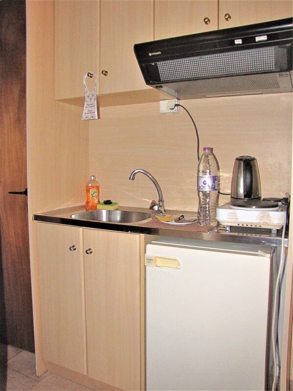 A compact kitchen with a sink, a small refrigerator, a kettle, and a bottle of water. - Gorgona Hotel (Alonissos)