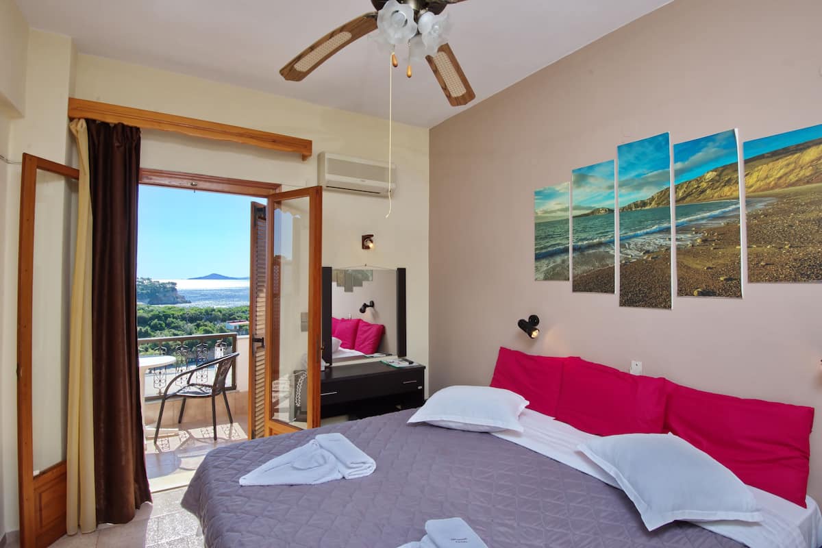 A hotel room with a bed, a balcony with a view, and a ceiling fan.