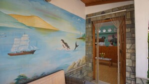 Quarto com um mural de paisagem marítima, porta de madeira que dá para uma cozinha e sofá de vime.