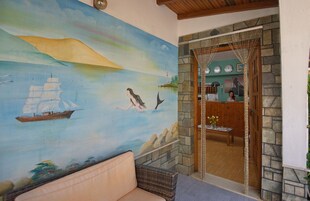 Una habitación con un mural de paisaje marino, una puerta de madera que da a una cocina y un sofá de mimbre.