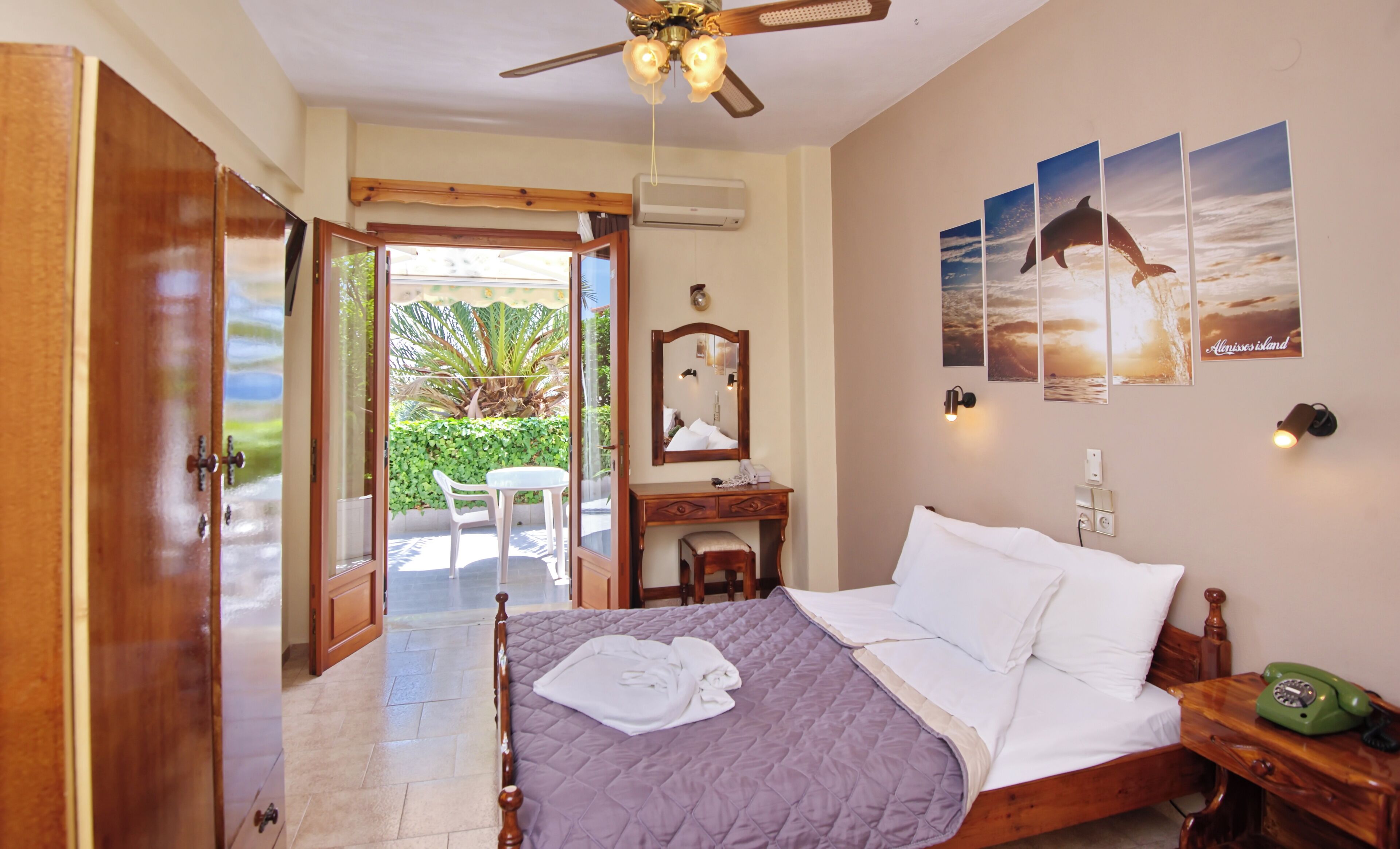 A bedroom with a bed, a desk, a chair, a wardrobe, and a balcony with a view of the sea.