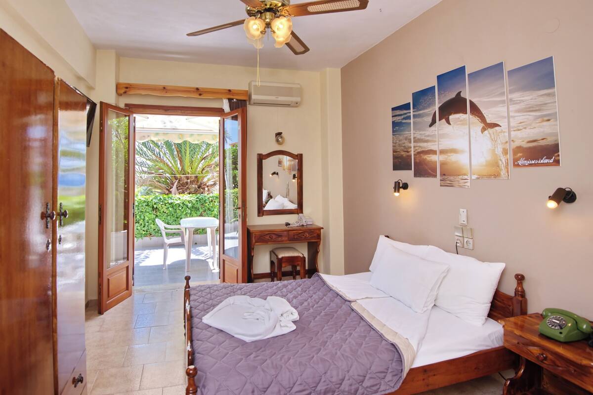 A bedroom with a bed, a desk, a chair, a wardrobe, and a balcony with a view of the sea.