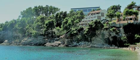 A coastal area with clear turquoise waters, rocky cliffs, and buildings with balconies overlooking the sea.