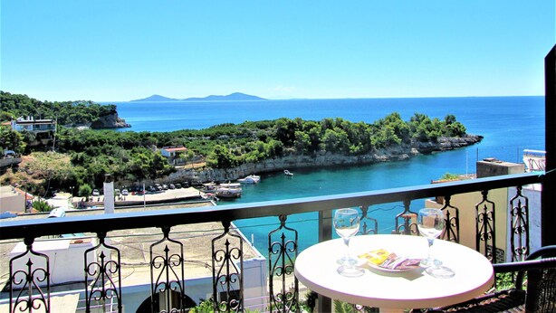 Uma varanda com mesa, vista para o mar e uma ilha ao longe.
