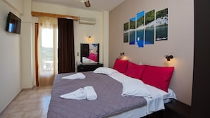 Quarto de hotel com cama grande, televisão de tela plana, varanda com cadeira e ar condicionado fixado na parede.