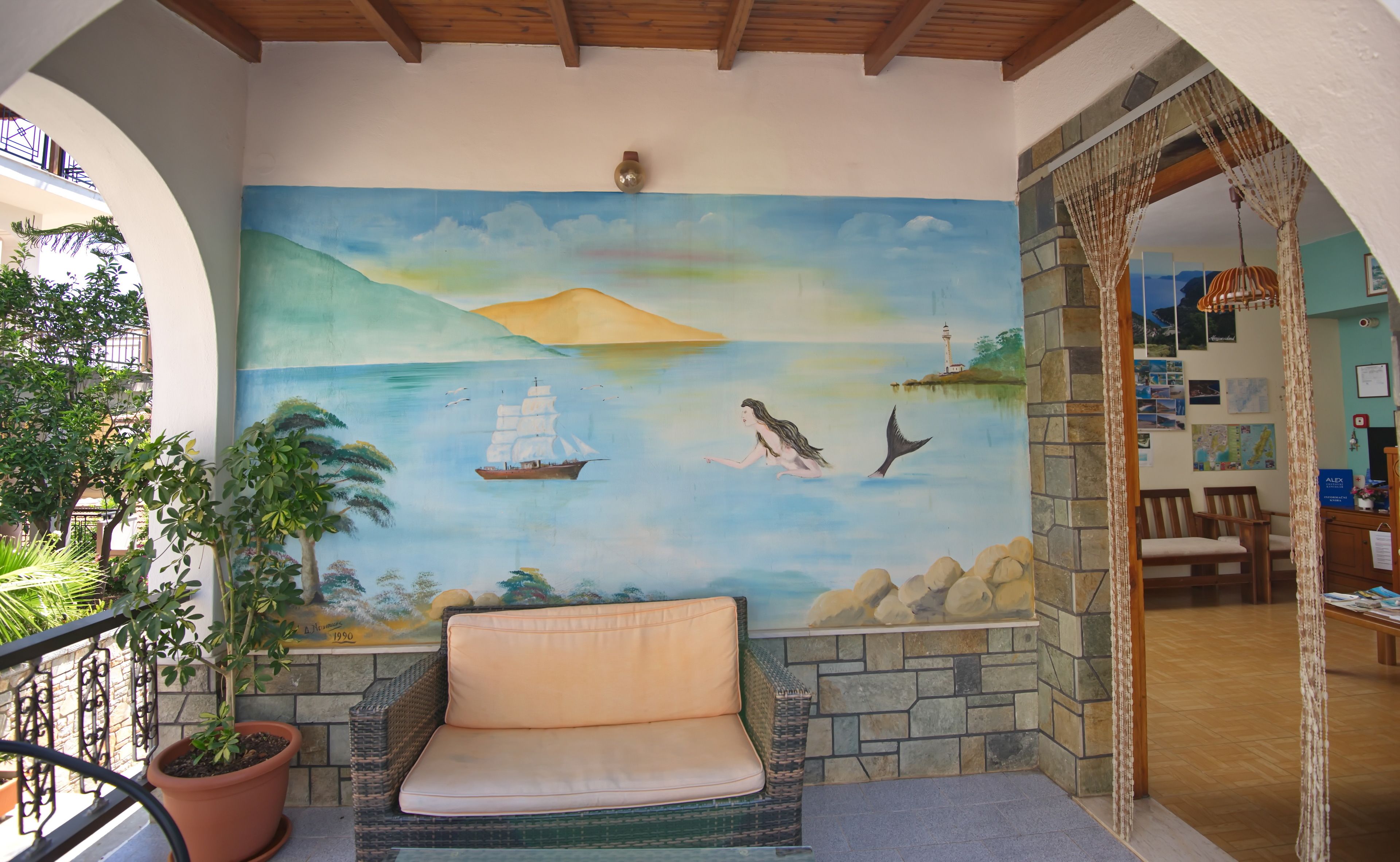 A room with a mural of a seascape, a wicker sofa, and a potted plant.