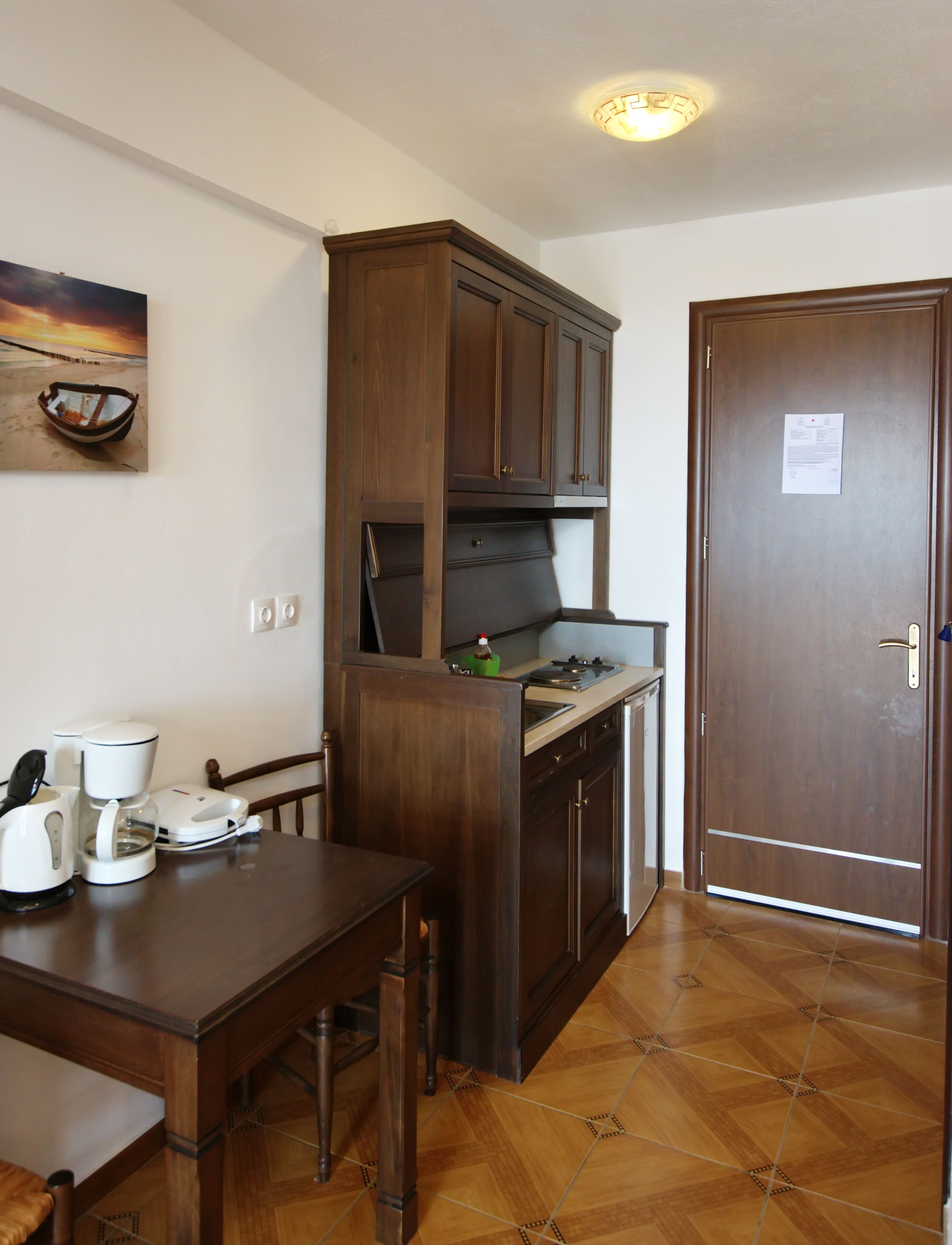 A compact kitchen with wooden cabinets, a dining table, and a coffee maker.
