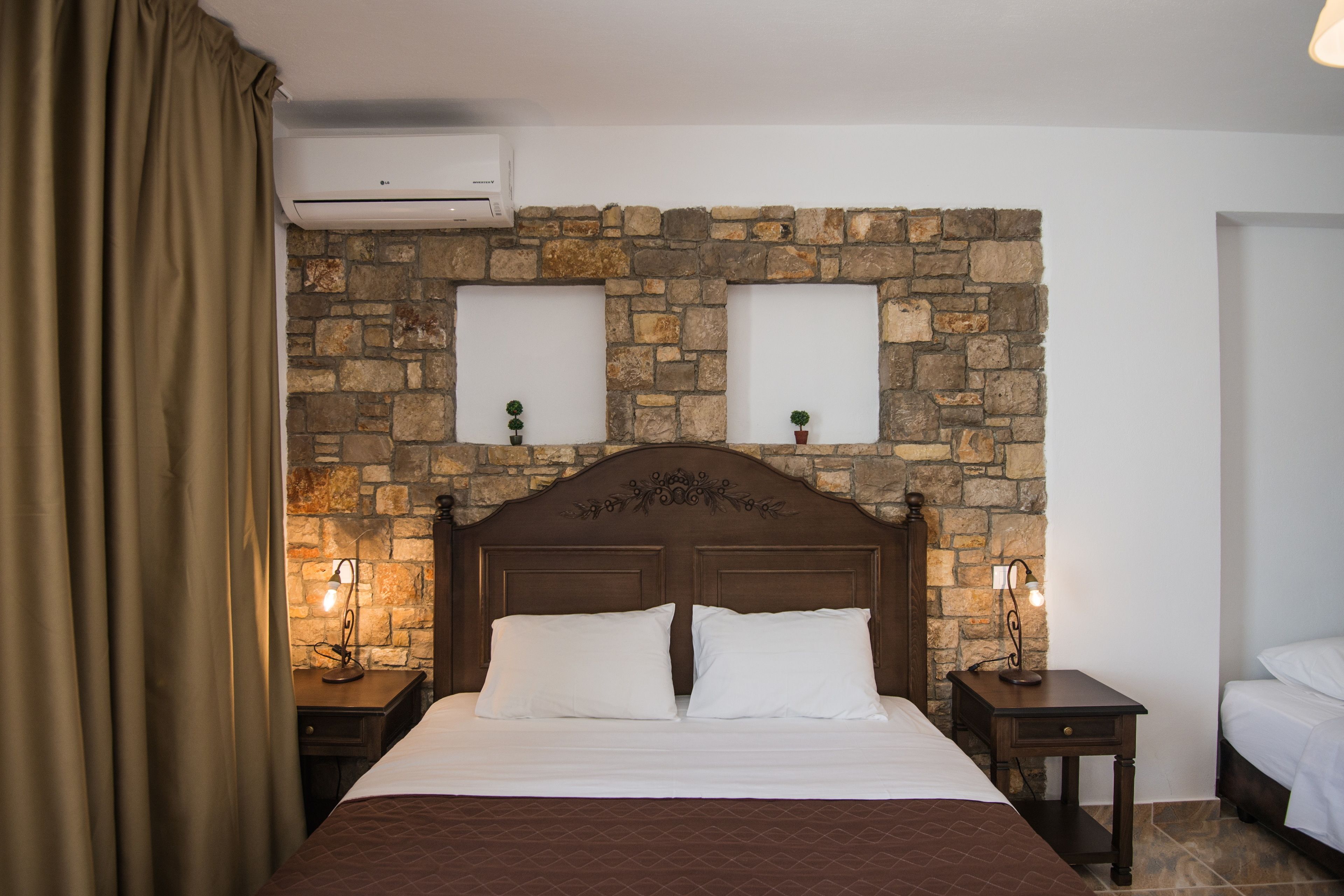 A bedroom with a stone wall, a wooden headboard, two bedside tables with lamps, and a bed with white bedding.