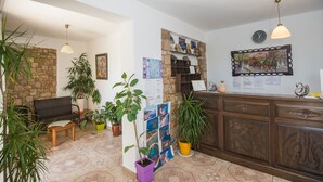 Uma área de recepção com parede de pedra, um banco de madeira, plantas em vasos, um quadro de avisos e um balcão de recepção de madeira.