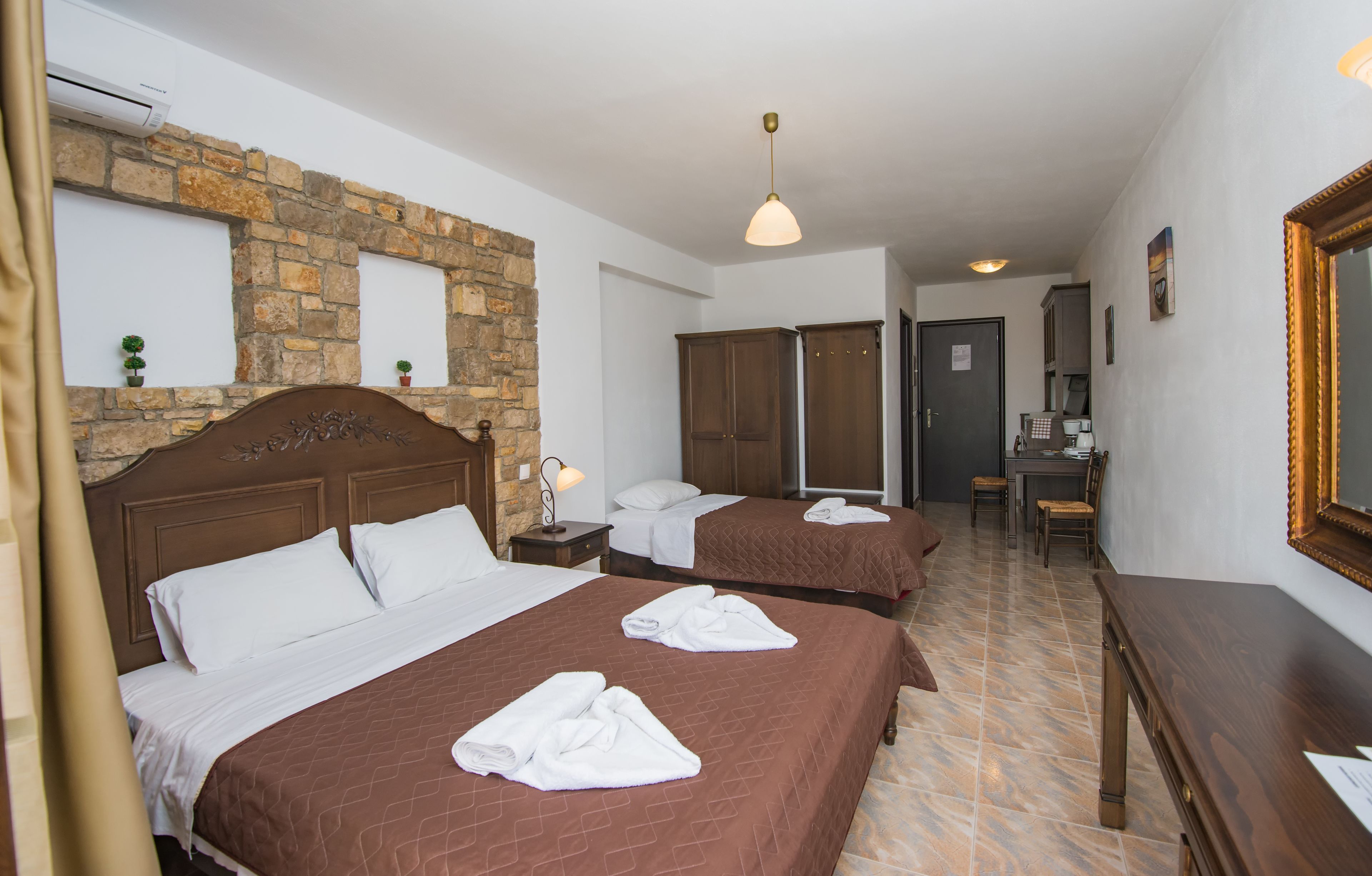 A hotel room with two beds, a stone wall, wooden furniture, and a tiled floor.