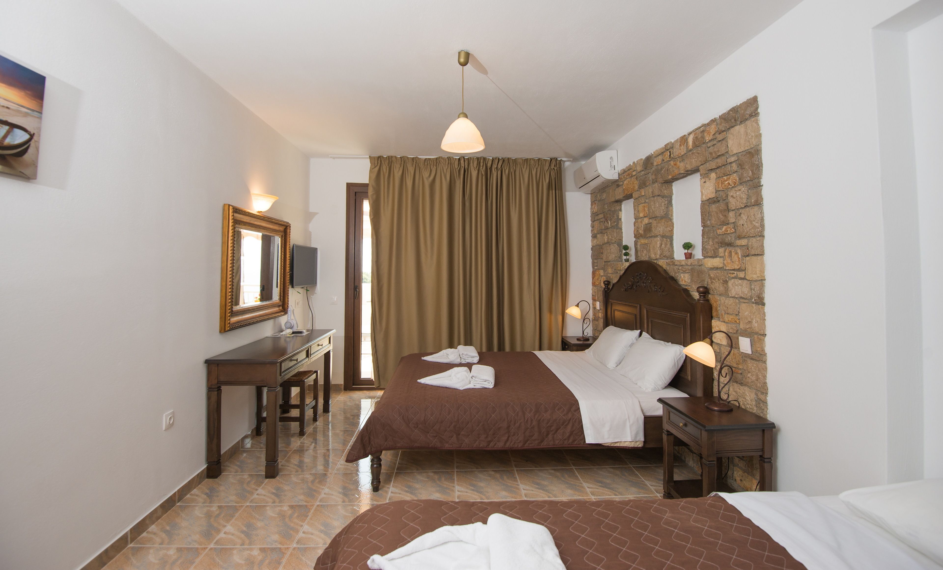 A hotel room with a bed, a desk, a chair, a television, and a stone wall.