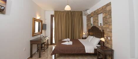 A hotel room with a bed, a desk, a chair, a television, and a stone wall.
