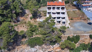 Vista aérea de um edifício com várias andares e varandas, localizado em um terreno rochoso com águas cristalinas em primeiro plano.