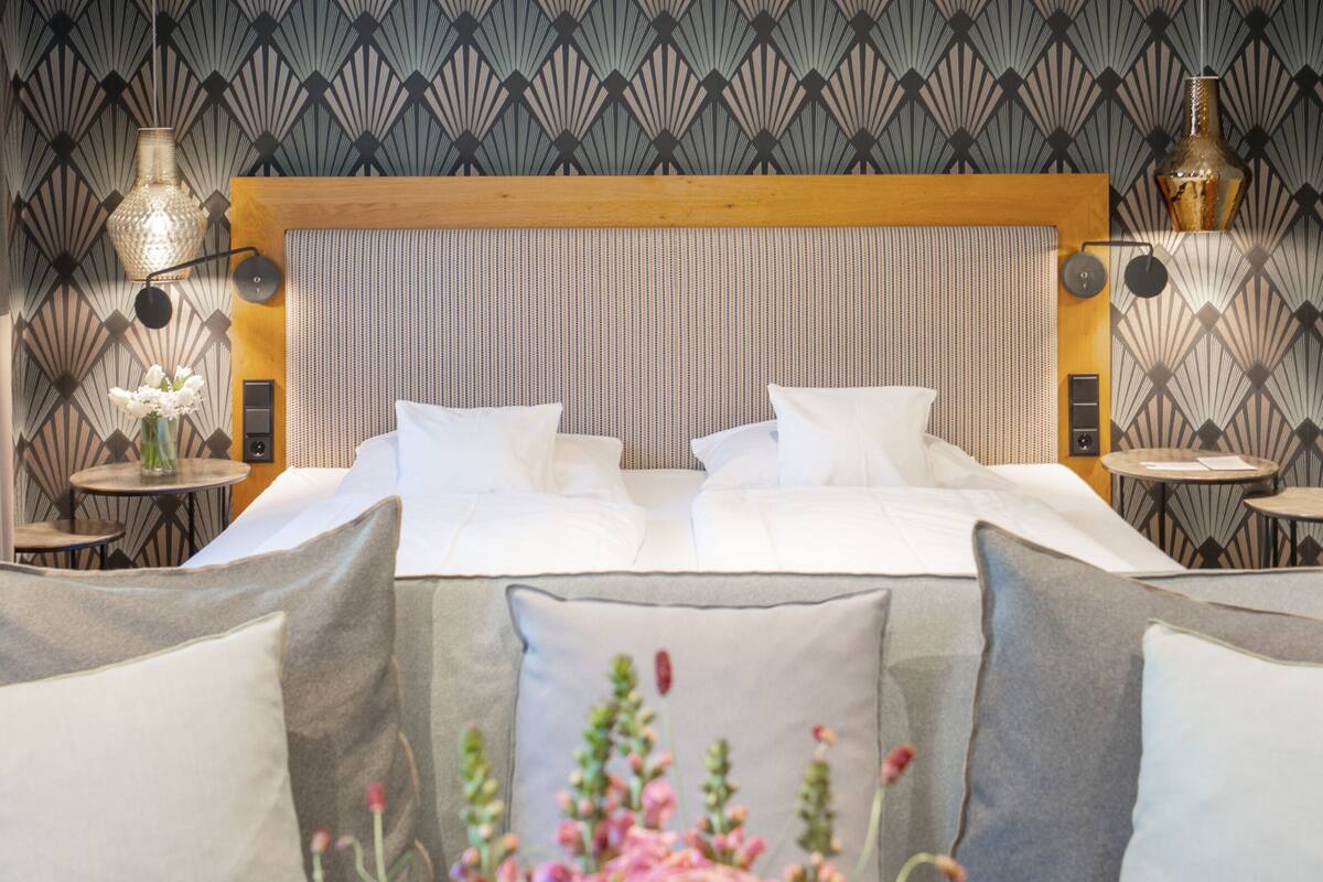 Una habitación de hotel con una cama grande, dos mesitas de noche, un cabecero y apliques decorativos en la pared.