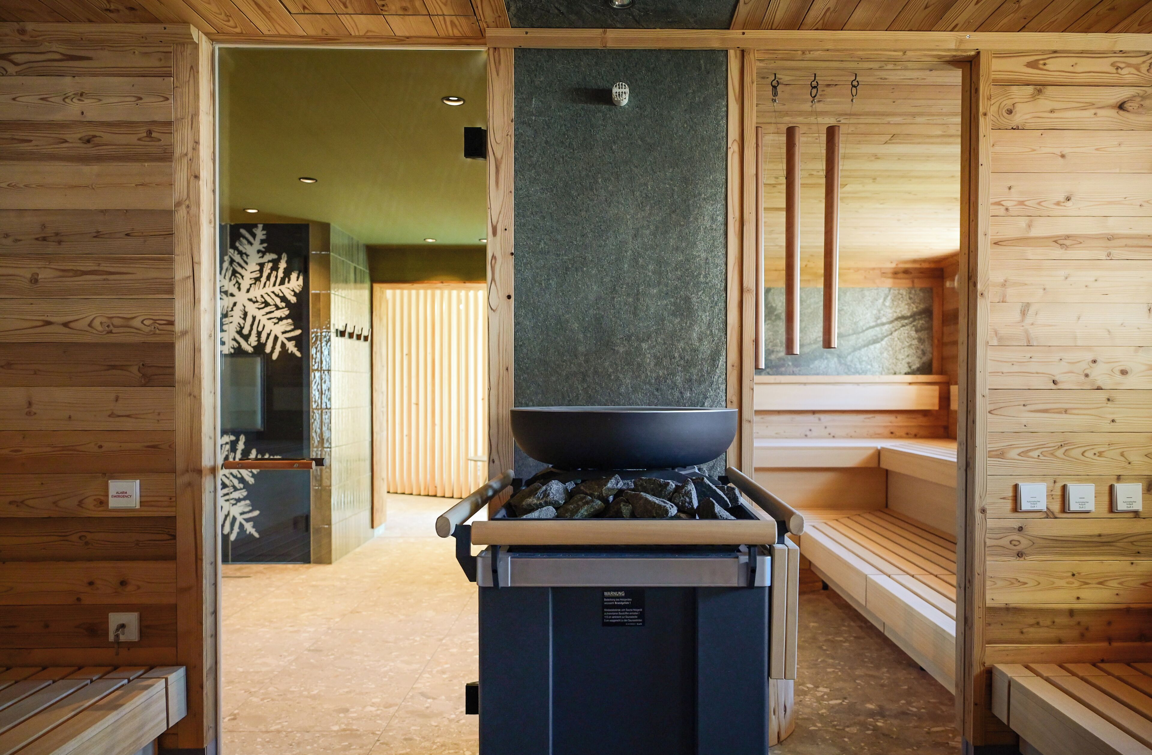 A sauna room with wooden benches, a large black sauna heater, and a wooden wall with a snowflake decoration.