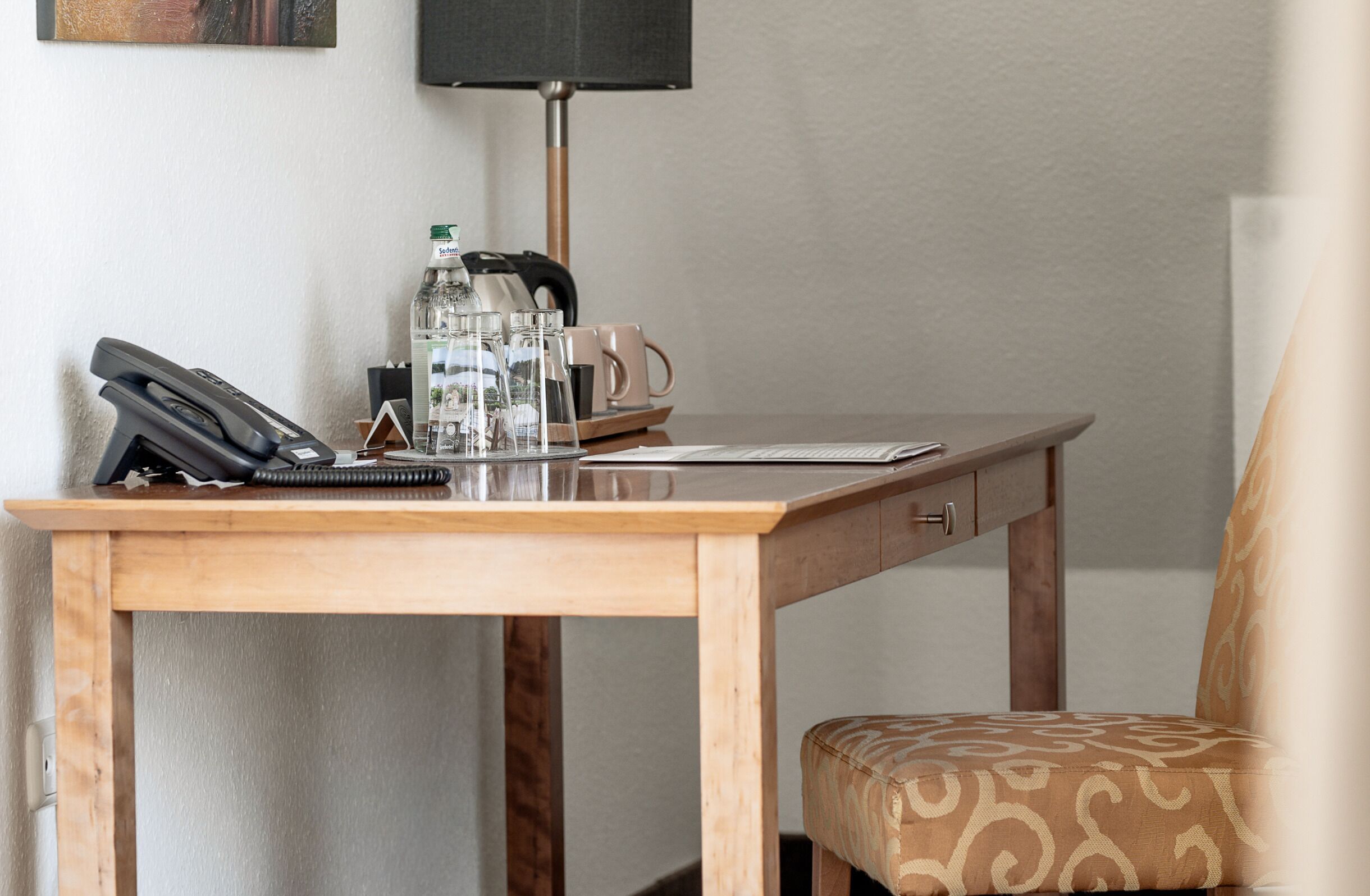 A wooden desk with a telephone, a mug, a bottle, and a lamp.