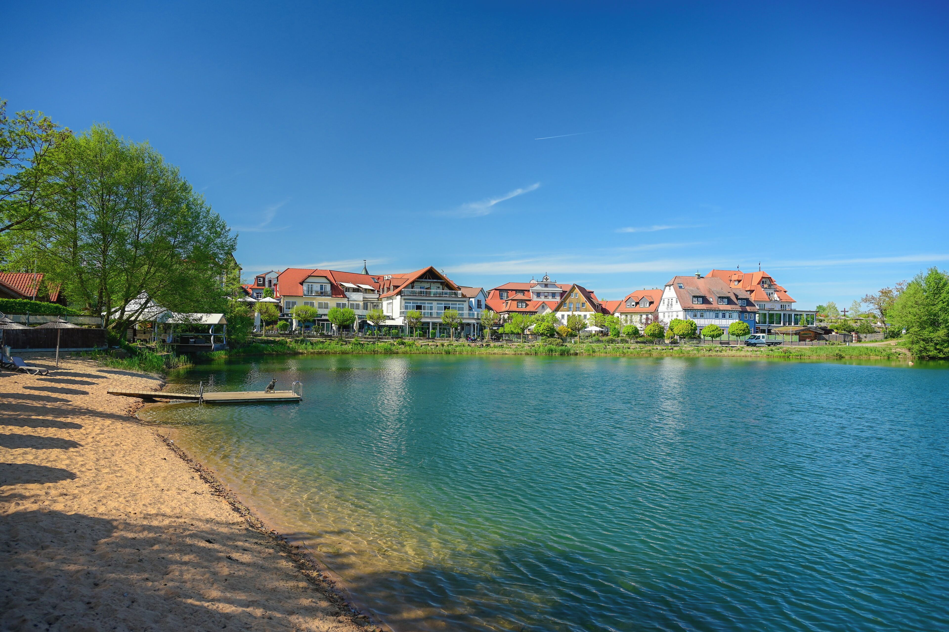 Uitzicht op een meer met huizen, een steiger en een zandstrand.