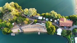 Vista aérea de una propiedad junto al lago con playa de arena, una zona de estar cubierta y un edificio con techo rojo.