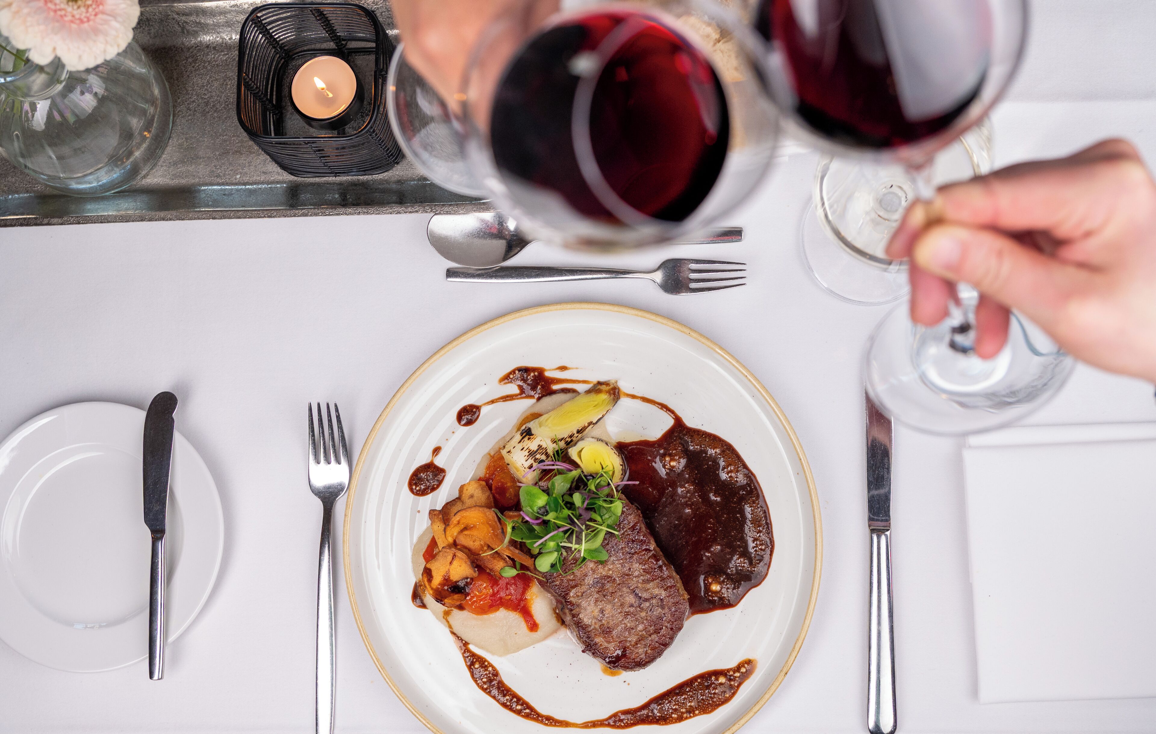 Una mesa de comedor con un plato de comida, cubiertos y una copa de vino tinto.