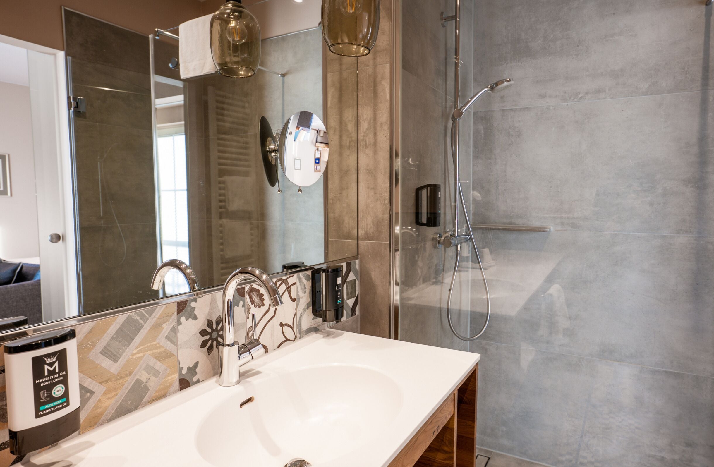 A modern bathroom with a large mirror, a white sink, a shower, and a towel rack.