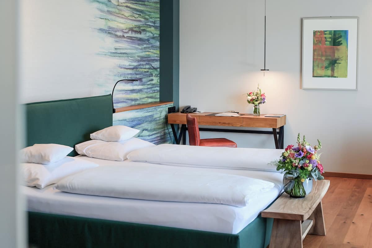 Habitación de hotel con cama, escritorio, silla, un jarrón de flores y un cuadro en la pared.