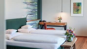 A hotel room with a bed, a desk, a chair, a vase of flowers, and a painting on the wall.
